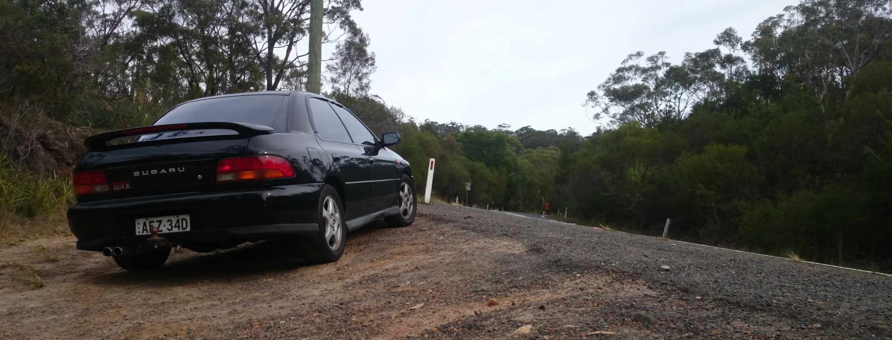 a black car is parked on the side of a dirt road