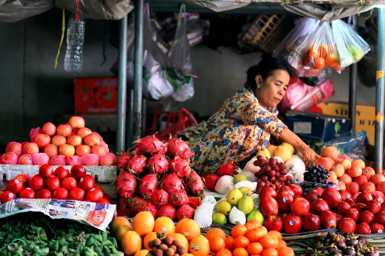 an older woman is standing at the fruit stand