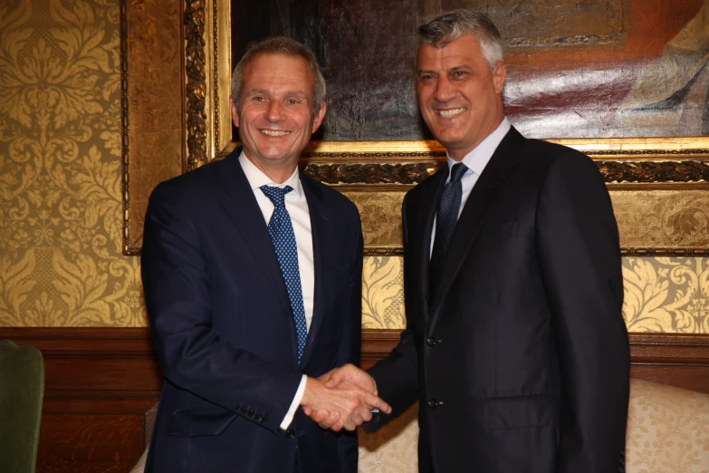 two men in business suits shaking hands in front of a painting