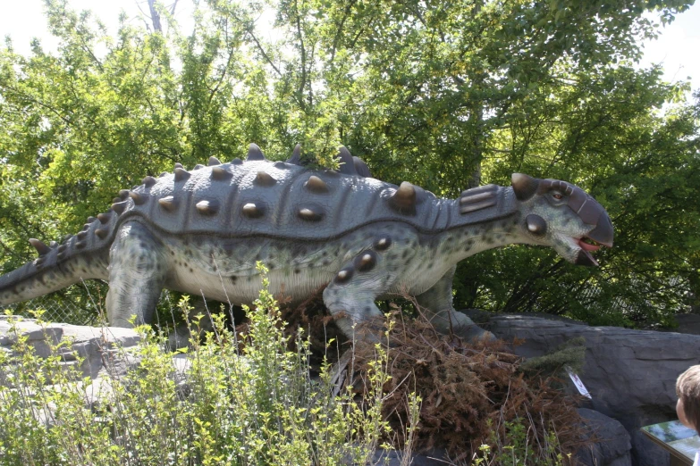 a statue of a dinosaur walking through a lush green forest