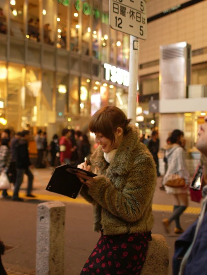 a woman in a brown coat standing on the sidewalk while looking at her phone