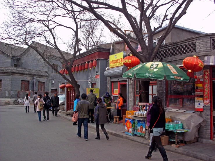 people walk around a shopping area that has red lanterns and green umbrellas