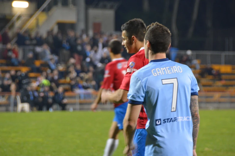 two teams in blue uniforms playing soccer, while people watch