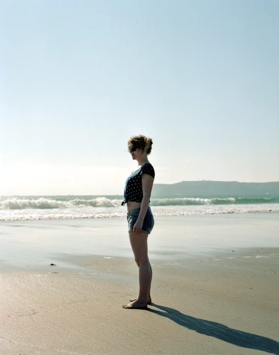 a lady standing on the beach near some water