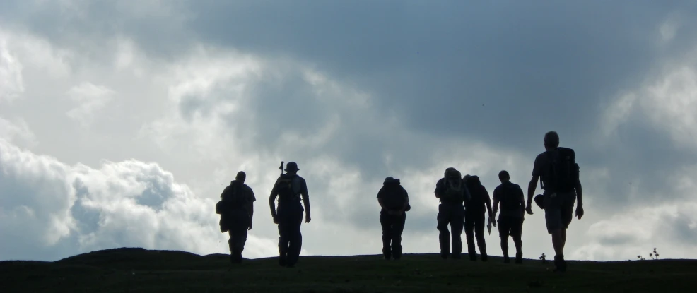 the silhouettes of six people stand on a hilltop under a cloudy sky