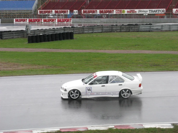 a white car on a wet track in front of an empty field