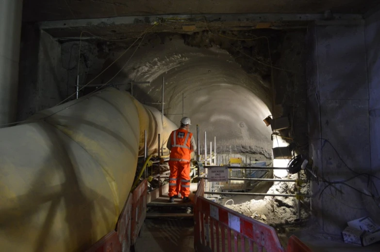 a worker in orange work clothes near a large pipe