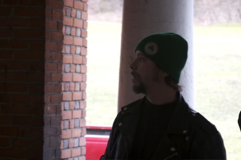 a man with a green hat on stands by a brick wall