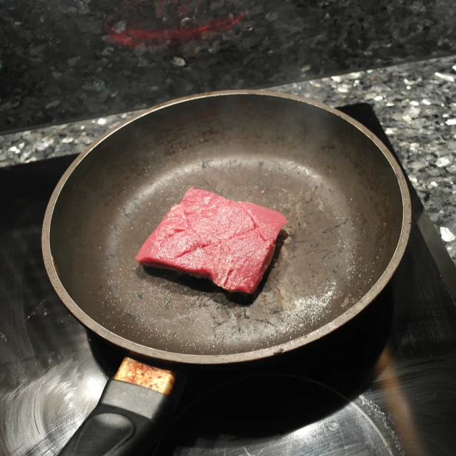 a piece of red meat sitting in a frying pan