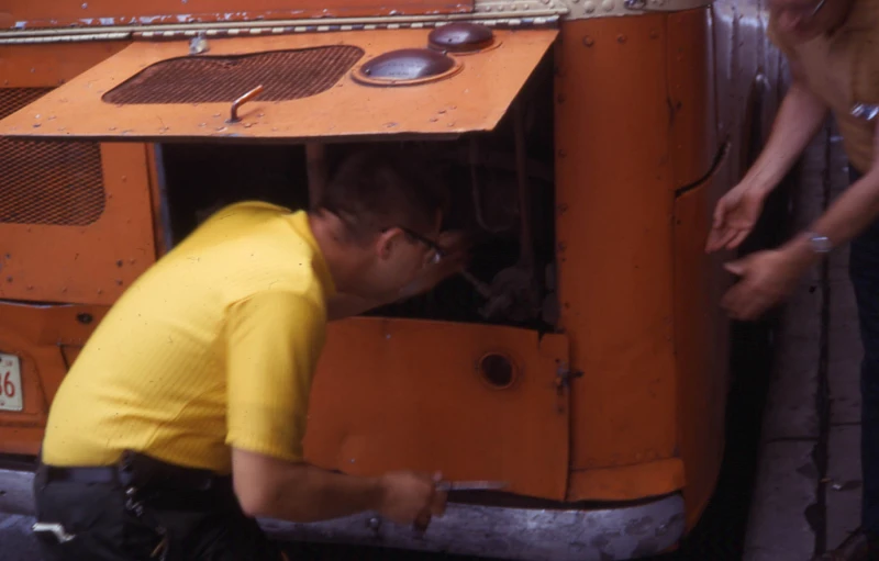 man with yellow shirt on, working on an orange truck