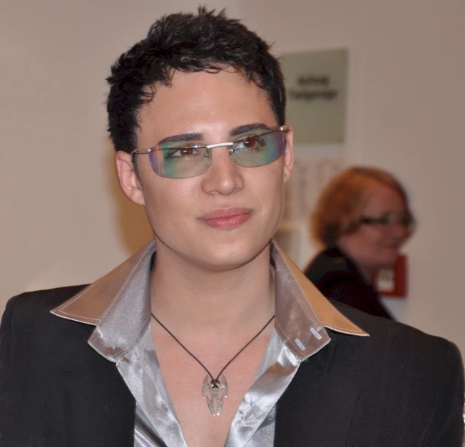 a man wearing a suit and sunglasses standing next to a white wall