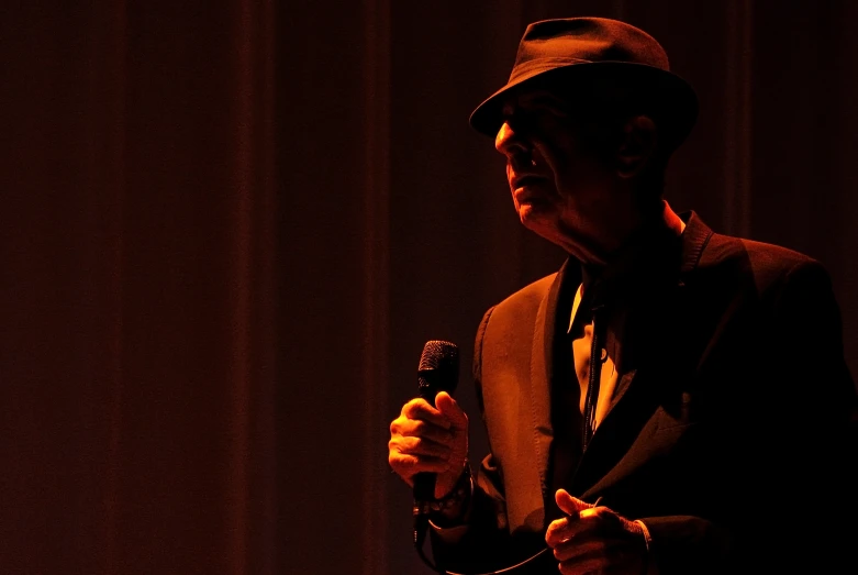 a man in suit and tie holding a microphone in front of a curtain