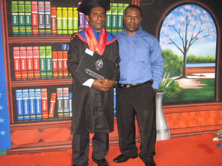 two men stand in front of a colorful bookcase with colored books