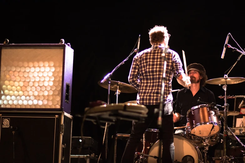 three people on stage with drum set and two other instruments