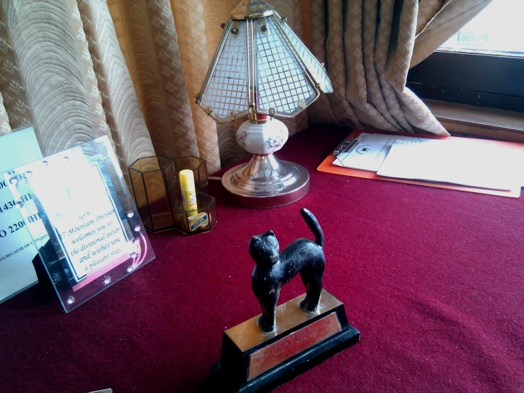 a black and grey cat on top of a book stand next to a lamp