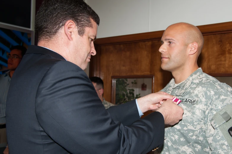 a soldier adjusting another man's tie in a suit