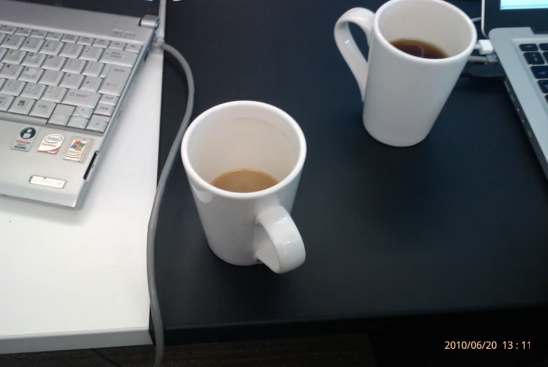 two white coffee cups next to a laptop computer