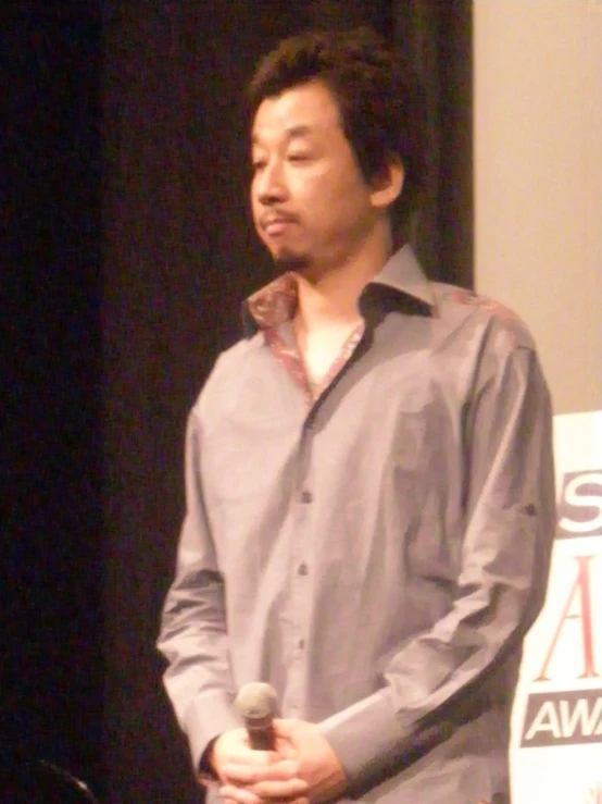 an asian man stands up in front of a microphone