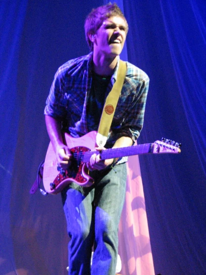 a man plays his guitar while singing into a microphone
