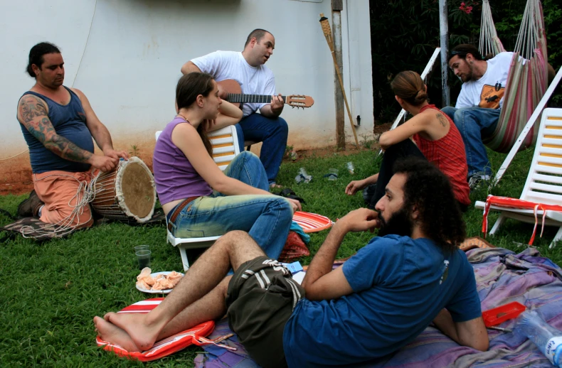 a group of people sitting and standing around on the grass