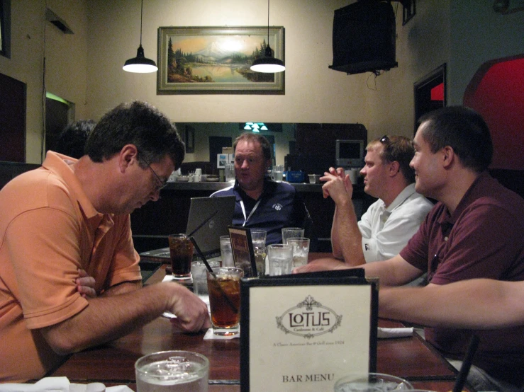 men are gathered around a table having drinks and looking at a laptop