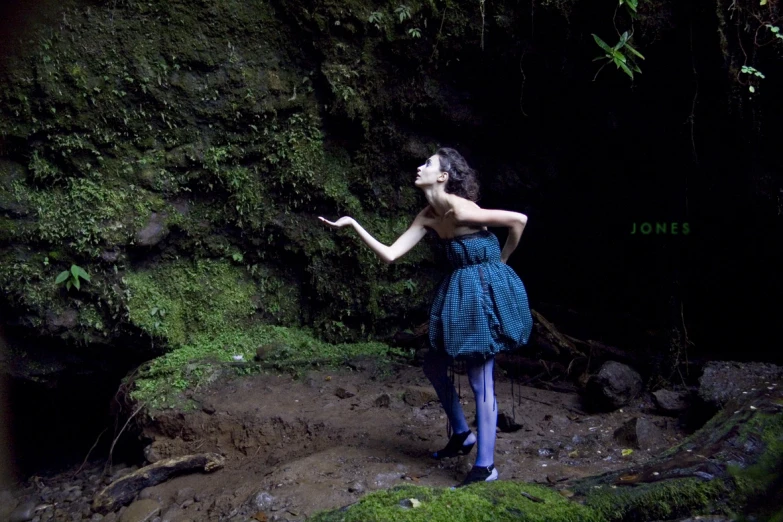 a model in a blue dress and a black handbag is standing in front of a dark forest