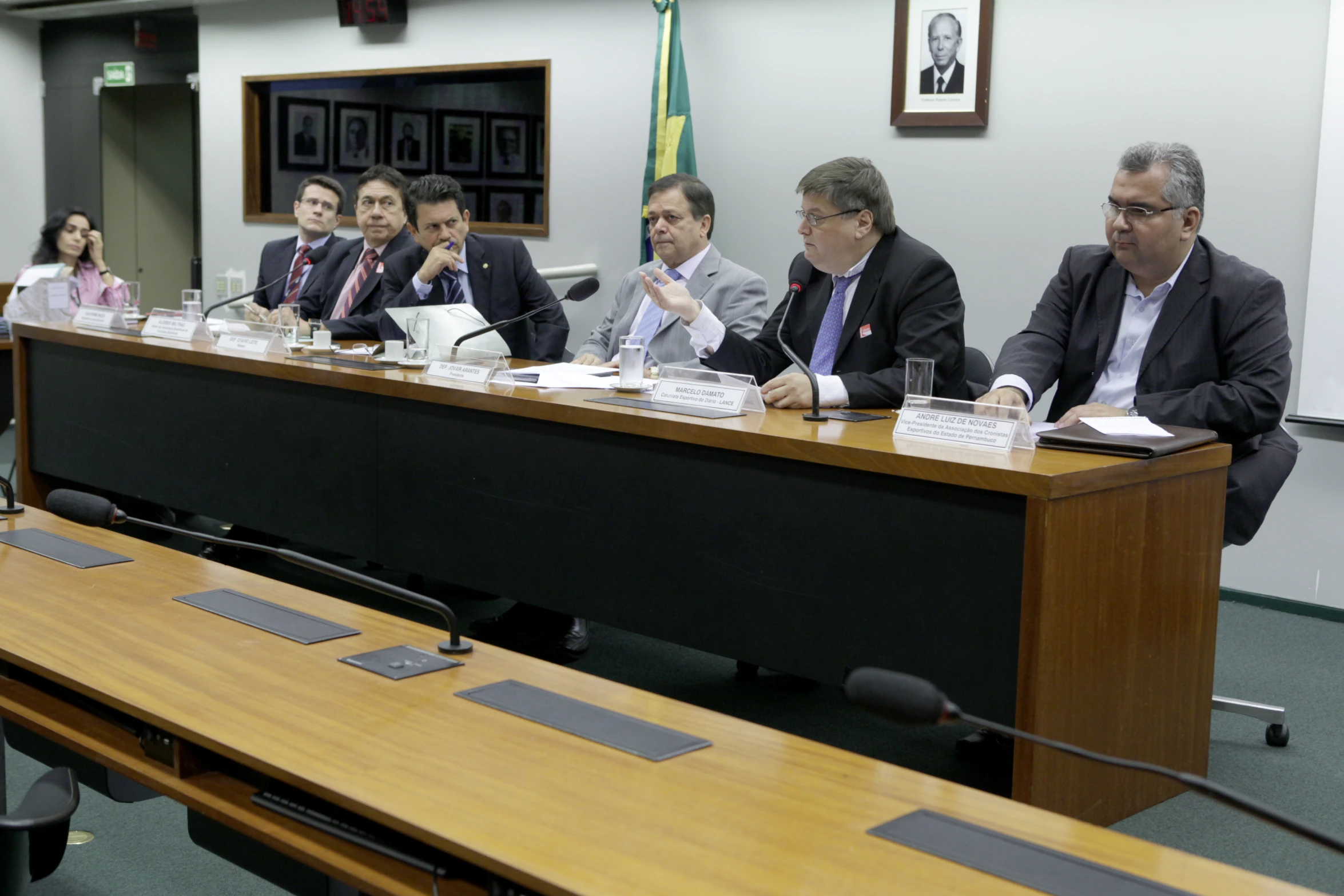 five men sitting at a long table with papers and talking