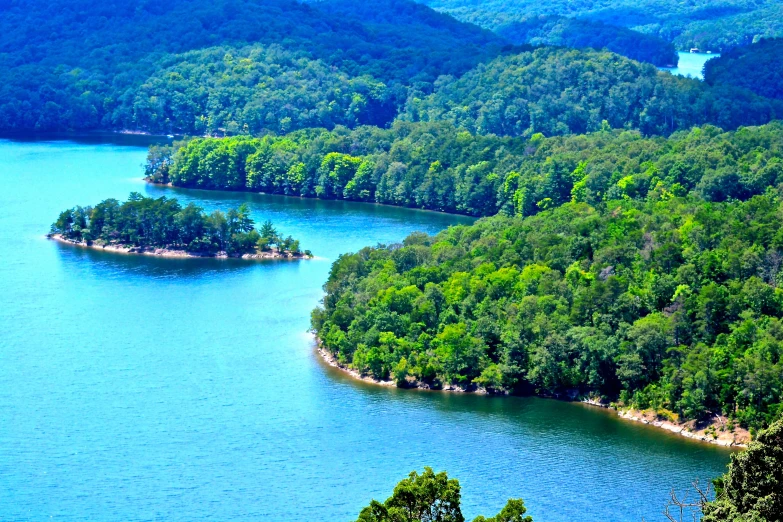 a group of mountains surrounded by water and green trees