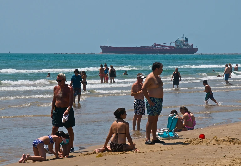 a lot of people at the beach and one big ship