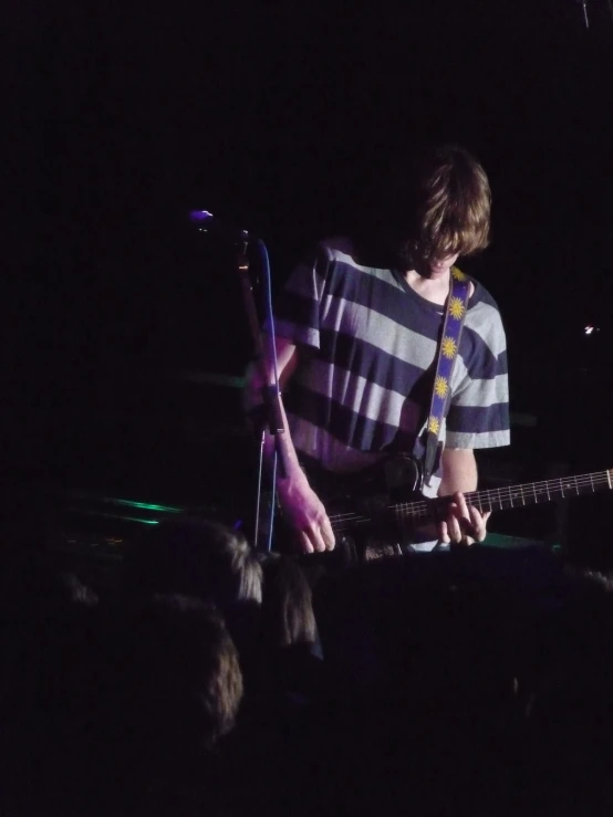 a man with long hair playing guitar in a dark stage