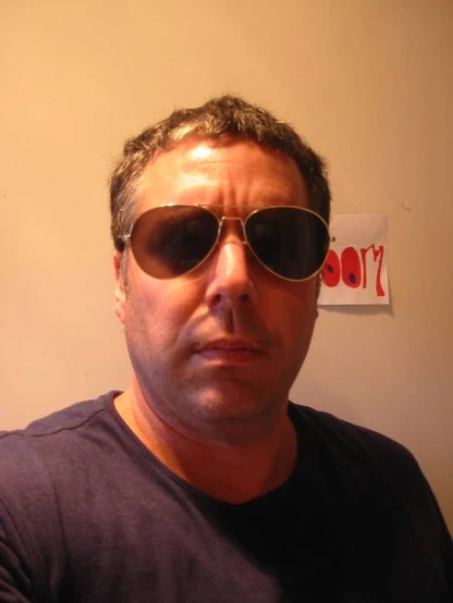 man in a t - shirt wearing sunglasses and a sign behind him
