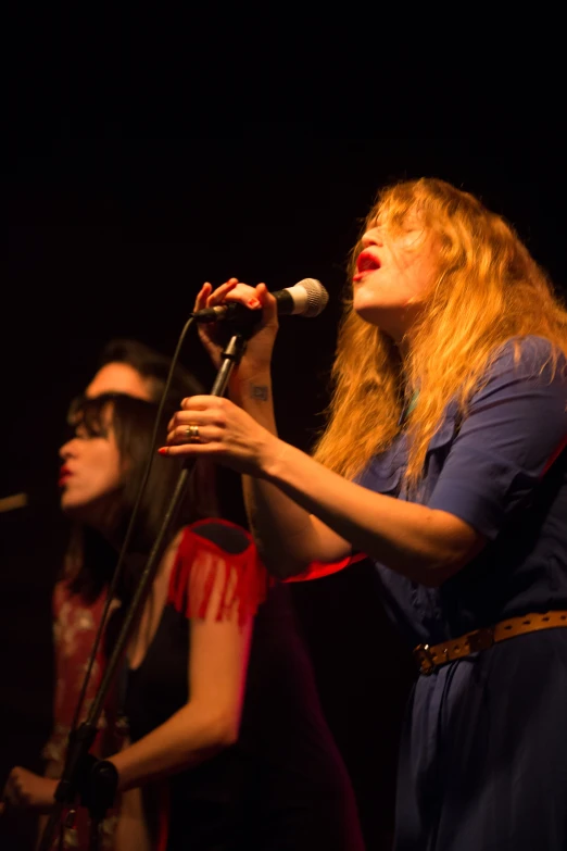 two women sing into microphones while one woman stands behind them