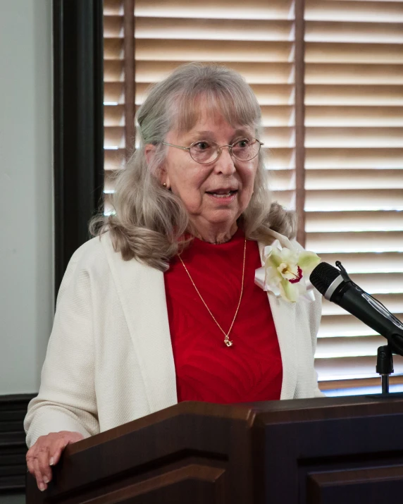 a woman wearing glasses and a red shirt stands in front of a microphone and microphone