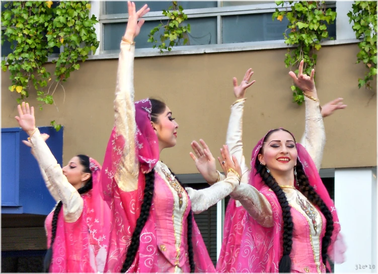 women in pink colored costumes hold their hands up and smile as they applaud a building