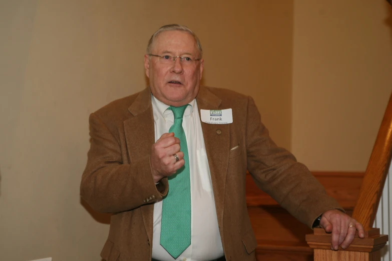 an older man holding a green tie with a badge attached