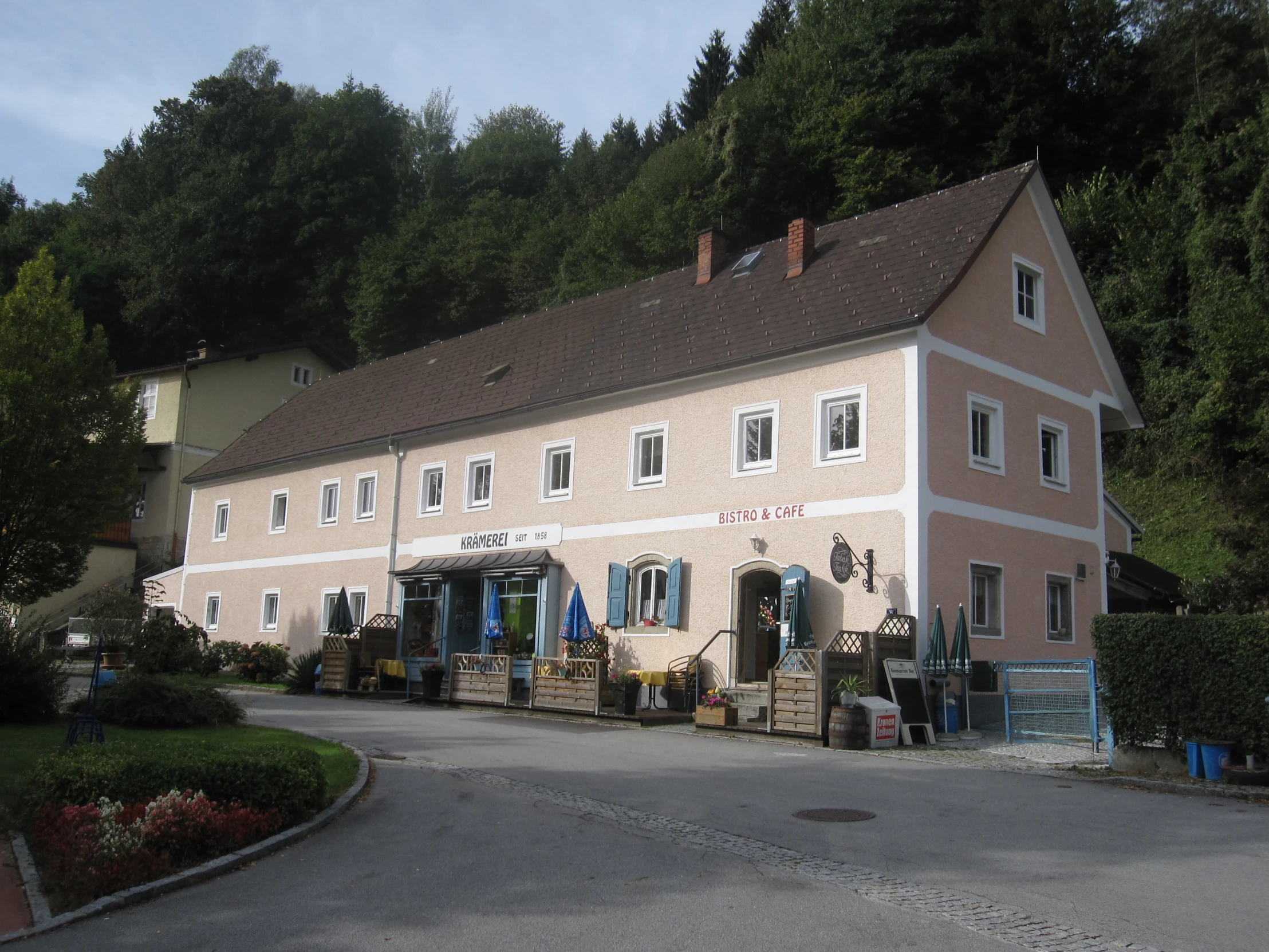 a two story brick building sitting beside a forest