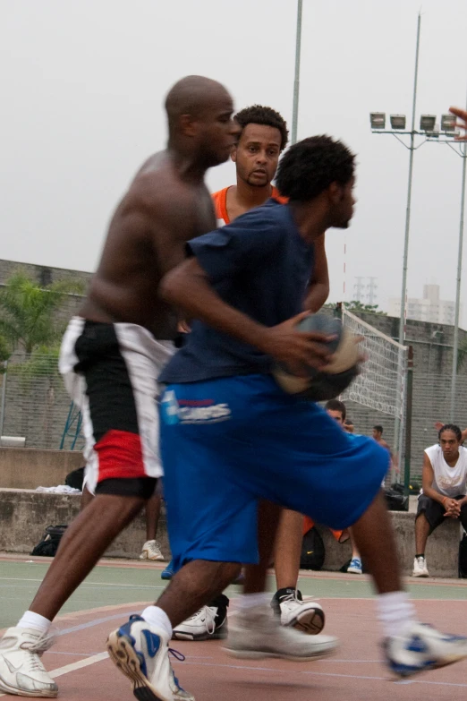 three men play basketball outside on a court