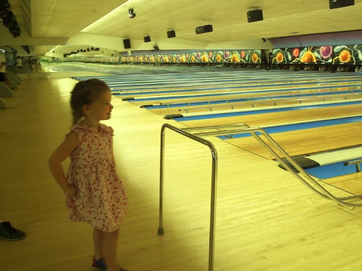 little girl stands at the end of a long line of bowling lanes