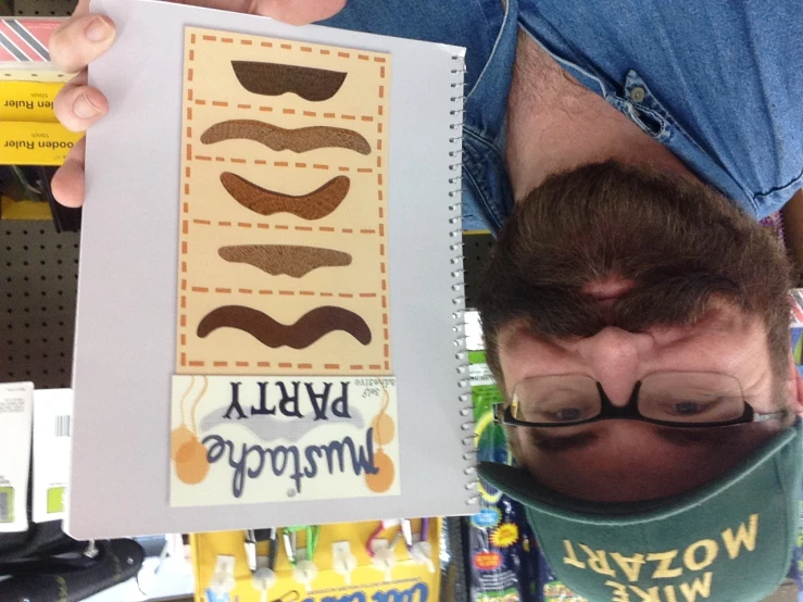 a bearded man in glasses and a cap holding up an image of mustache party