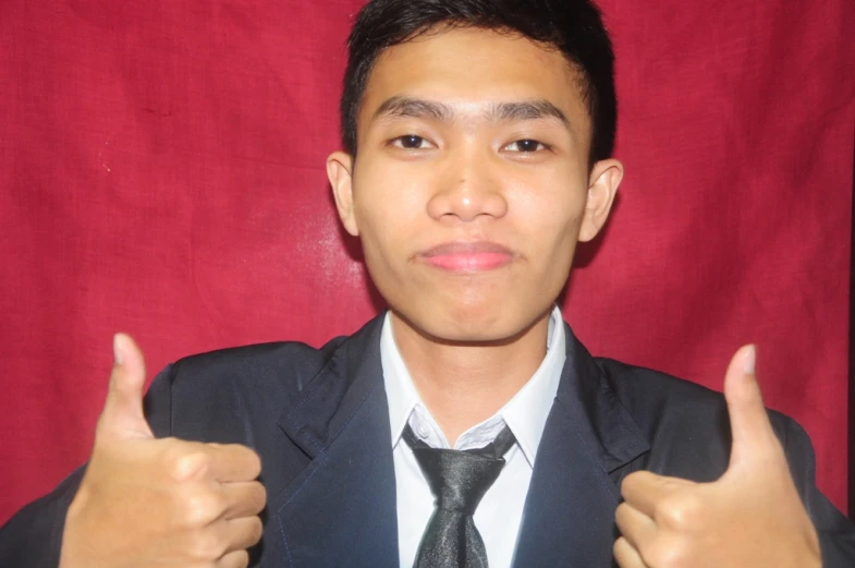 an asian man wearing a suit gives thumbs up