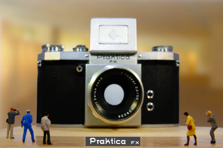miniature people standing next to an old camera