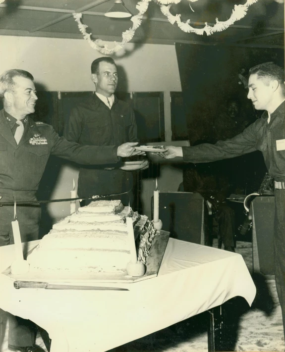 two men in uniforms handing out a cake on a table