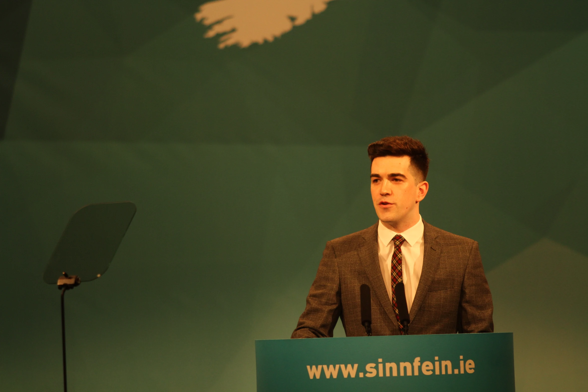 man in suit speaking from behind a podium with microphone