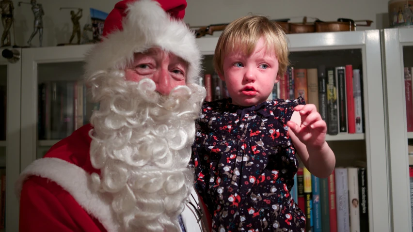 a little boy next to santa clause with a surprised look on his face