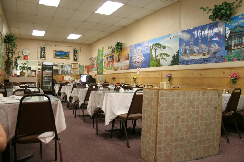 a table with chairs and white cloths sits between two walls in the dining room of a restaurant