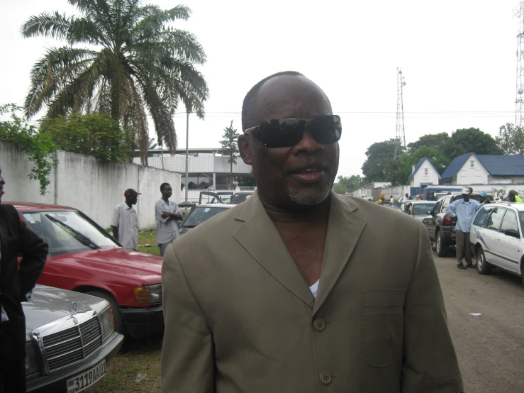 a man in a suit and sunglasses stands by parked cars