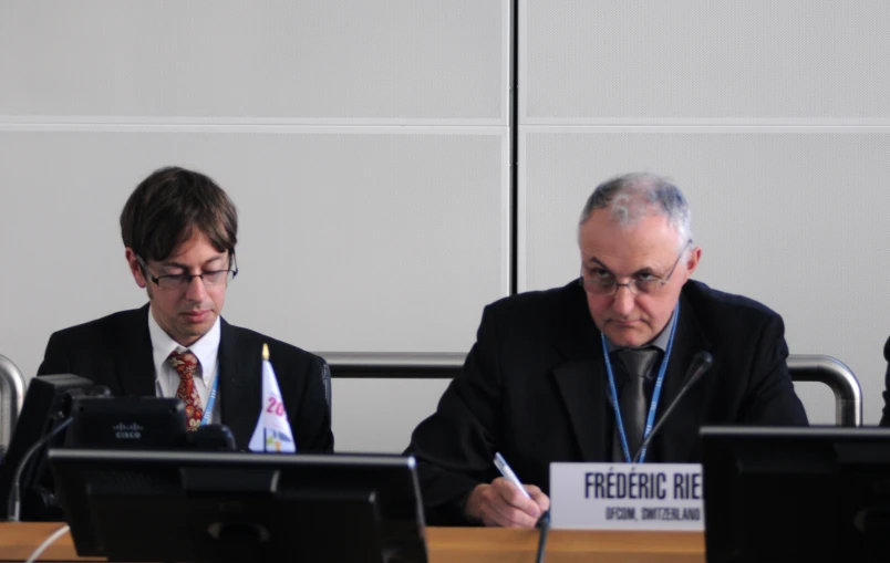 two men in business attire sitting at desks with computers