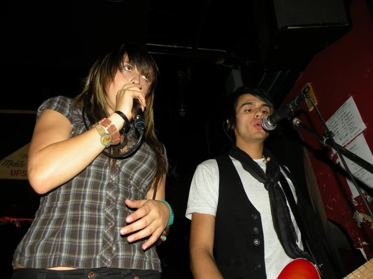 two people playing guitar and singing into microphones