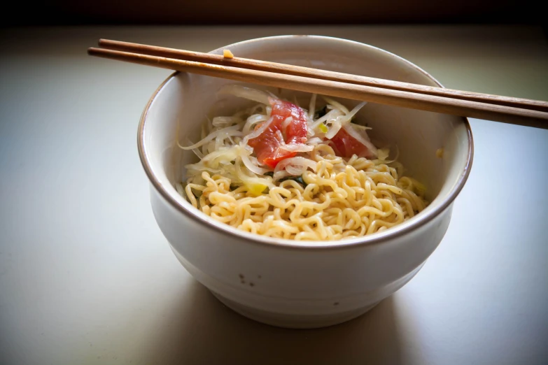 a bowl with noodles and vegetables and chopsticks