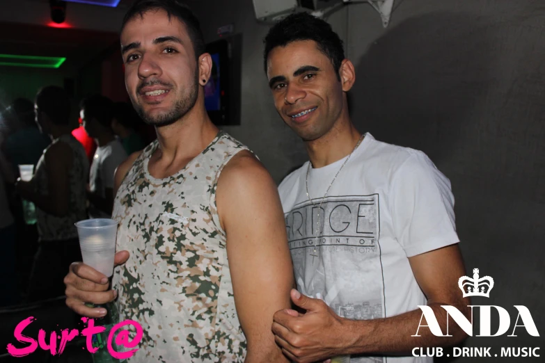 two men holding onto cups with a party in the background